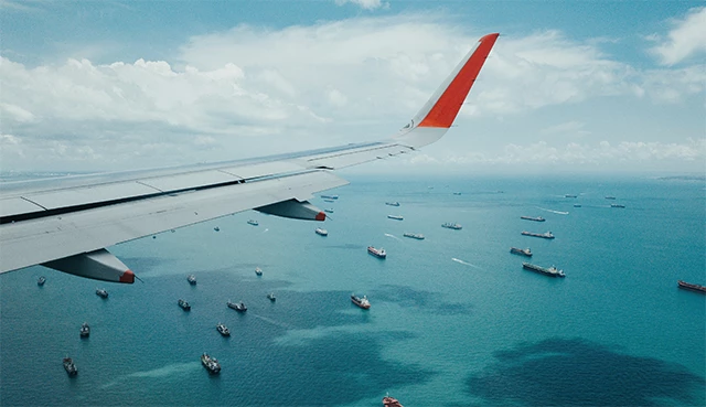 Flügel eines Flugzeugs über einem Meer mit zahlreichen Schiffen, repräsentiert die Logistiklösung portaZa der OdiSys GmbH.
